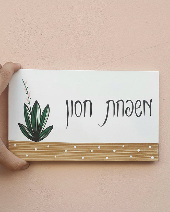 שלט לדלת כניסה עם צמח ירוק וכיתוב אישי בעבודת יד על בסיס עץ טבעי