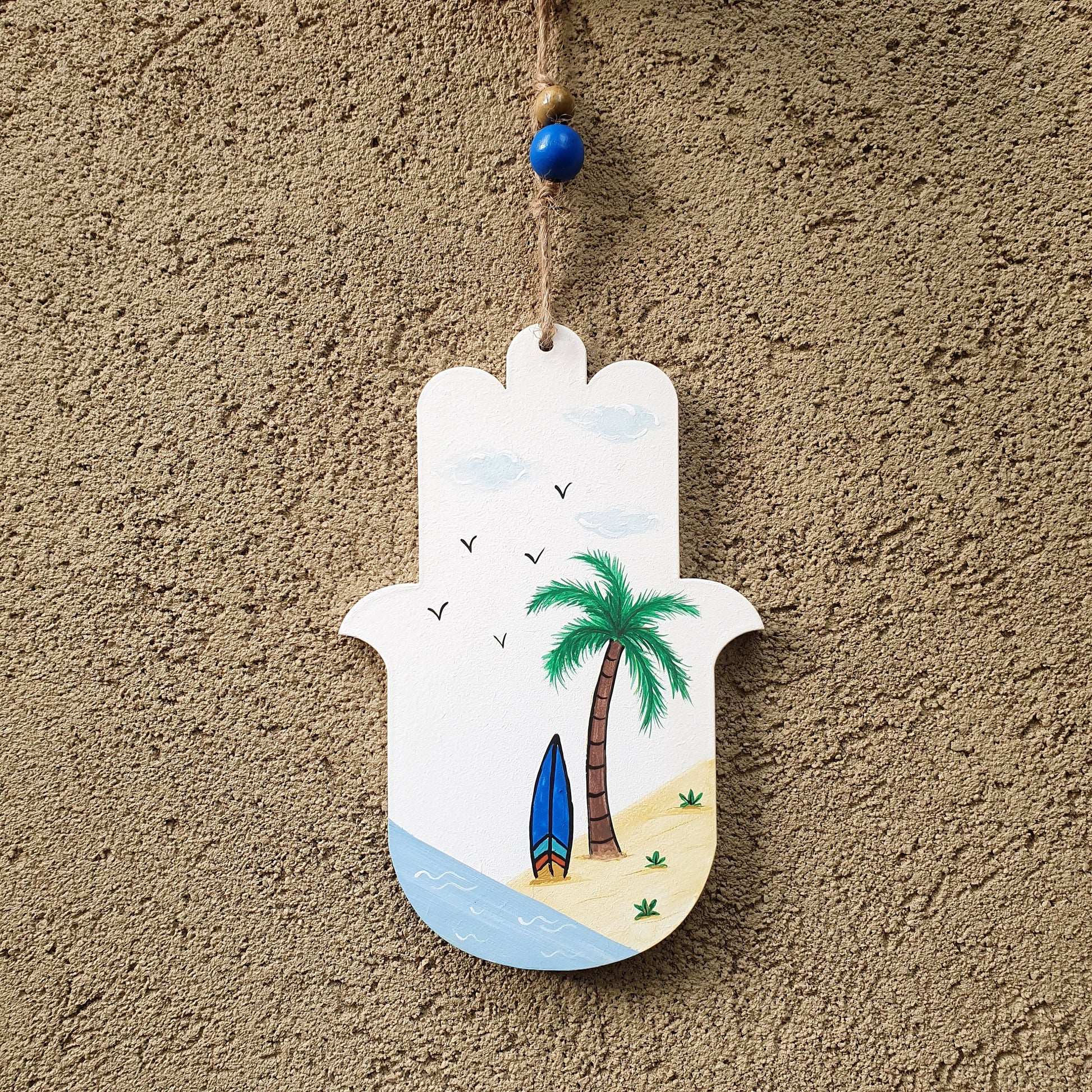 חמסה מעוצבת לקיר בעבודת יד עם ציור דקלים וים תלויה על דלת כניסה לבית באור טבעי